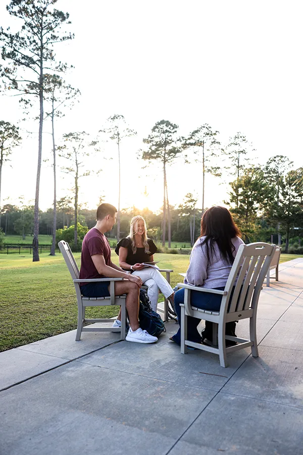 Three PCOM South Georgia students studying on the rear porch with the sun peering through tall trees