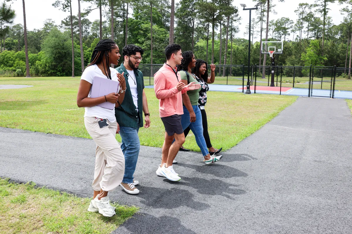 PCOM South Georgia students smiling and walking along a path with a basketball court in the rear