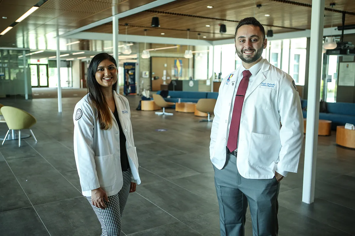 Two medical students smiling in their white coats within PCOM South Georgia's lobby