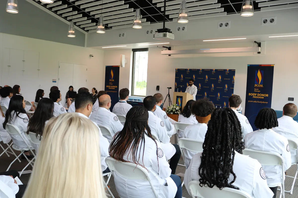 SGB/DeLoache room setup with rows of chairs and medical students in white coats participating in a Body Donor Memorial service event