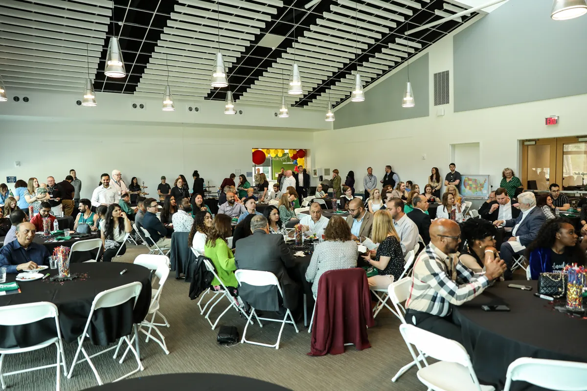 Lots of people sitting and mingling and round tables and chairs during an event at PCOM South Georgia