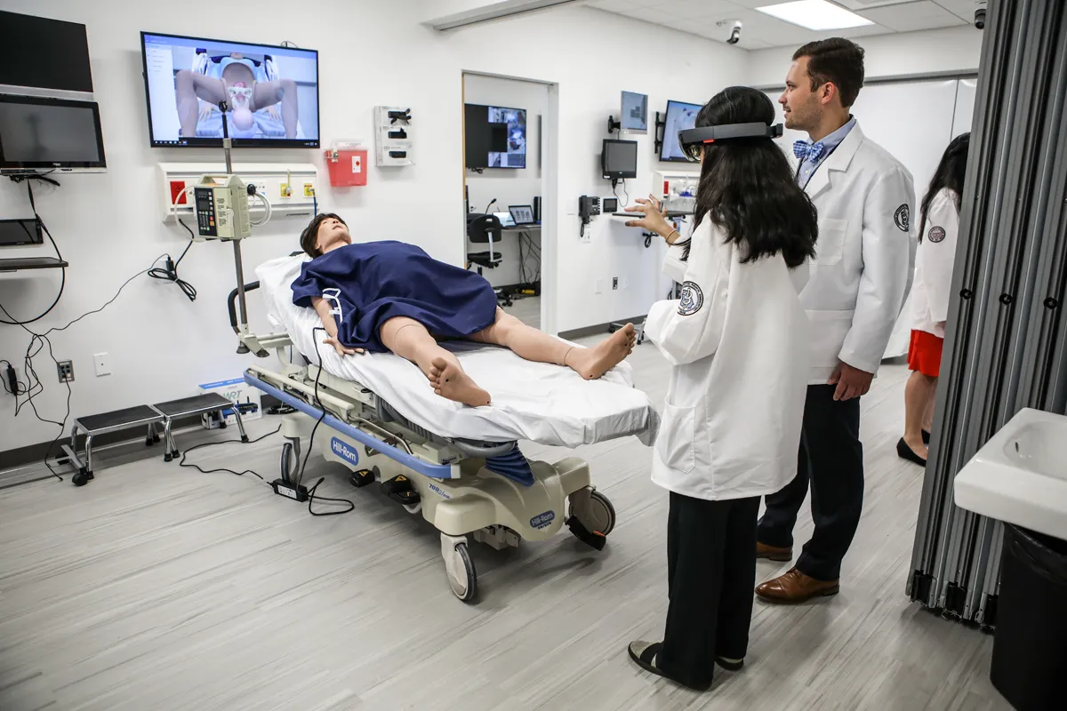 DO students using VR equipment next to a pregnant mannequin in the Simulation Center