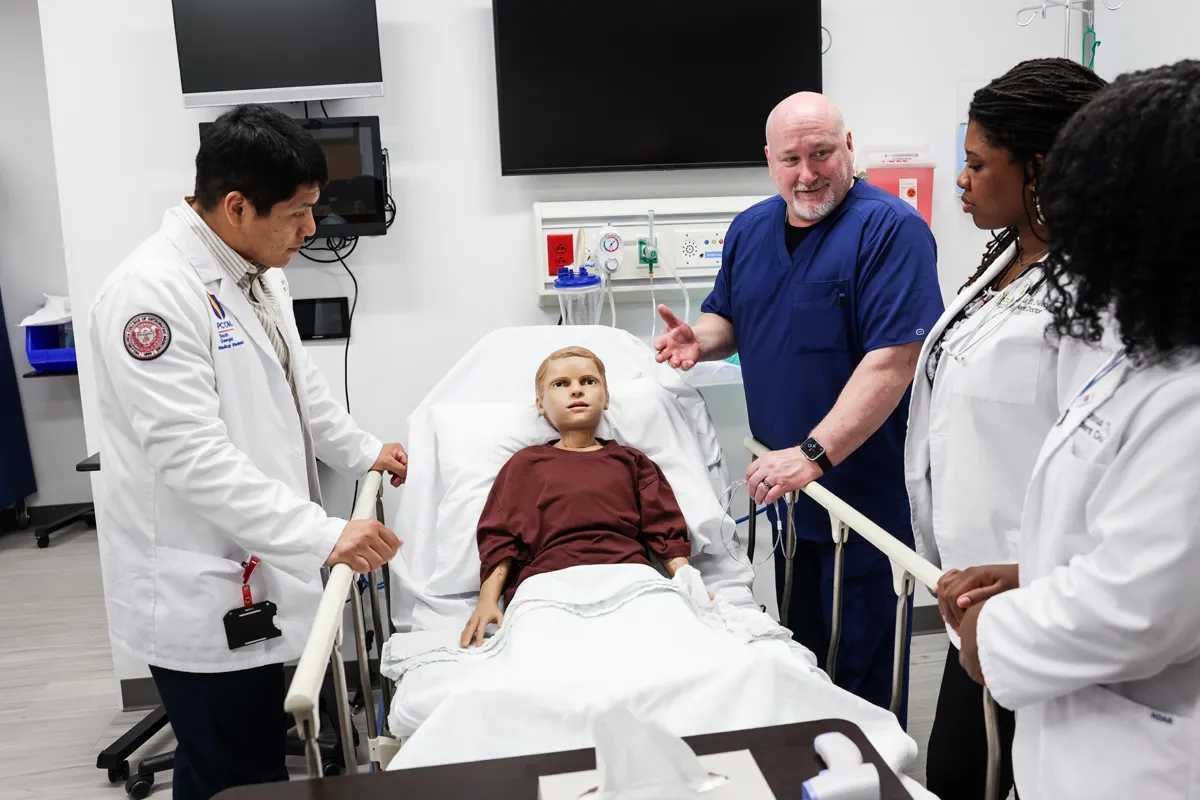 Students and faculty smiling and talking over a child mannequin in the Simulation Center