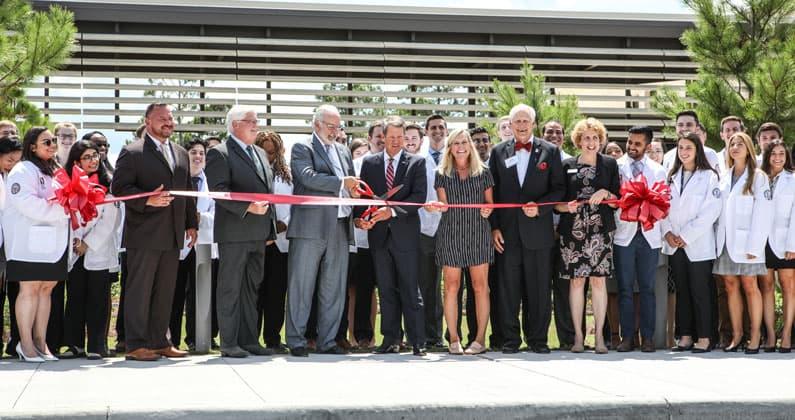 Gov. Kemp, PCOM South Georgia executive leaders and first year medical students smile and cut the ribbon in front of PCOM South Georgia.