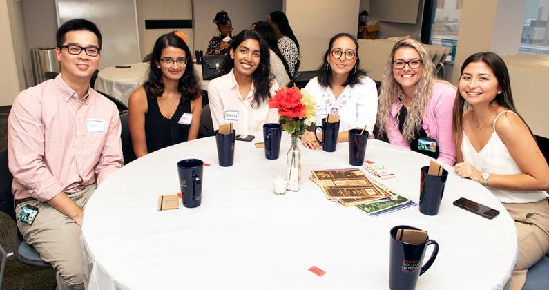 PCOM students smiling while sitting at a dining table during the Diversity Dinner event.