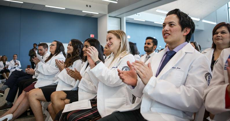 Seated medical students clap in the audience.