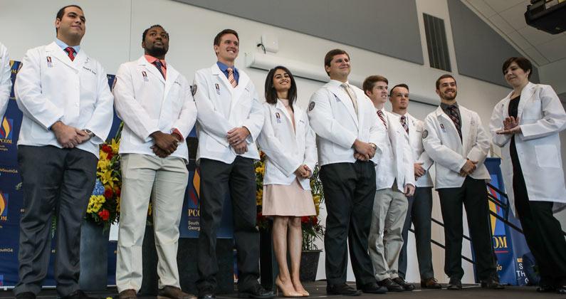 Medical students in white coats stand on stage at the white coat ceremony.
