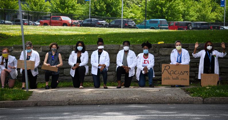PCOM students, faculty and staff kneel along the sidewalk and hold signs in support of the Black Lives Matter movement.
