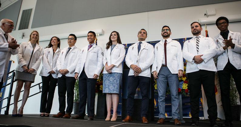 PCOM South Georgia DO students smile on stage seats during the white coat ceremony in October 2019.