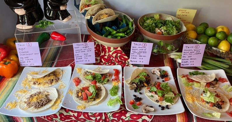 Table spread of various Mexican food dishes including four different tacos and two salads.