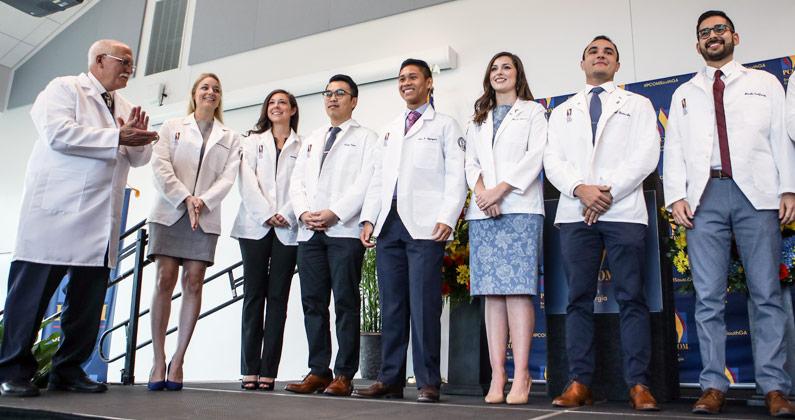 Medical students and George Fredrick, MD, stand on stage during the physician white coat ceremony at PCOM South Georgia.