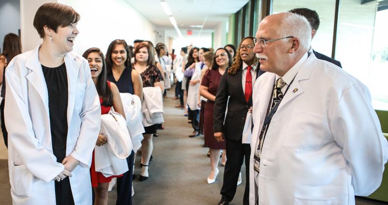 George Fredrick, MD, laughs with faculty and students in a PCOM South Georgia hallway.
