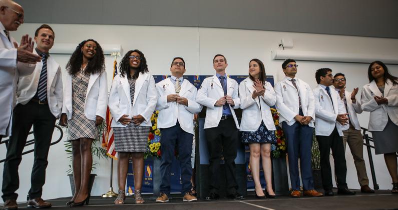 PCOM South Georgia DO students wear their white coats on a stage during the White Coat Ceremony.
