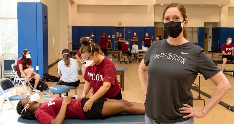 Dr. Noto Bell poses in front of PCOM DO students conducting physical exams in an OMM lab.