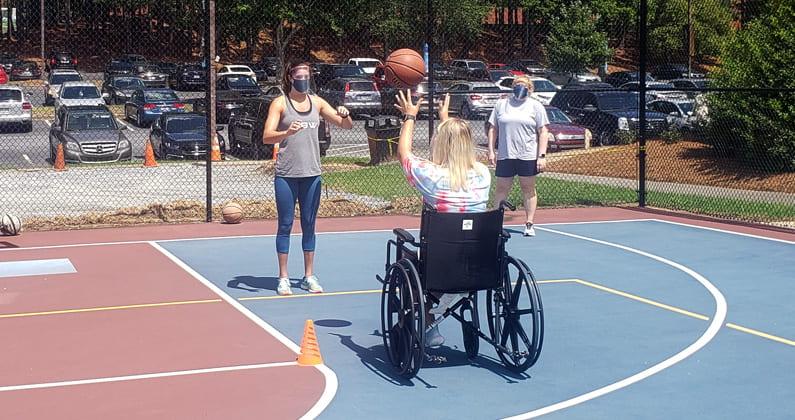 A PT student in a wheelchair has a pass with a basketball with a classmate.