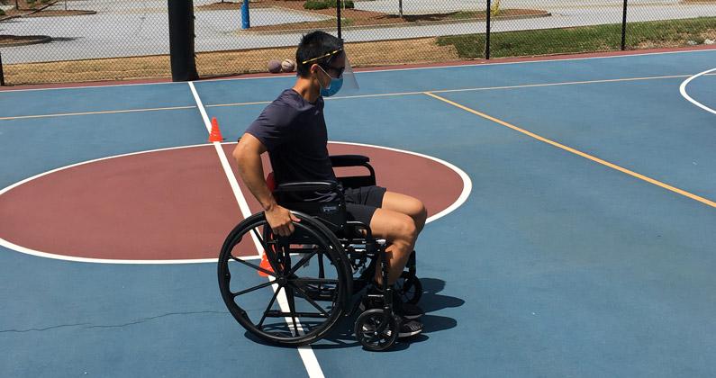 A physical therapy student rolls a wheelchair on a basketball court so he can learn more about sports opportunities for persons with disabilities.