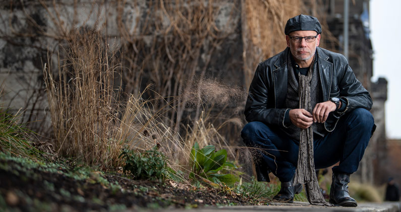 Gregory McDonald, DO, crouches on top of a stone wall outside of Eastern State Penitentiary.