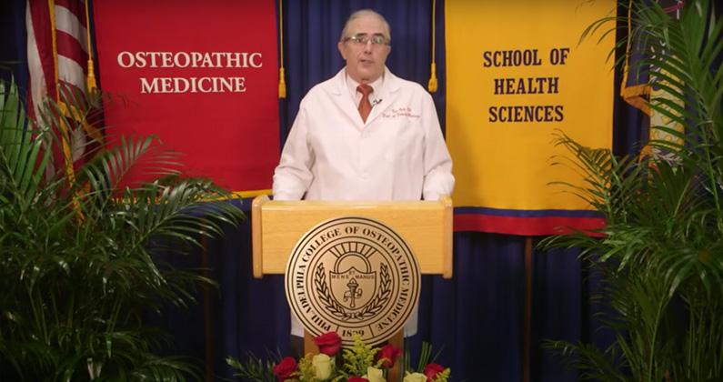 Provost Kenneth Veit, DO, MBA, FACOFP, addresses PCOM students from a podium during the virtual white coat ceremony.