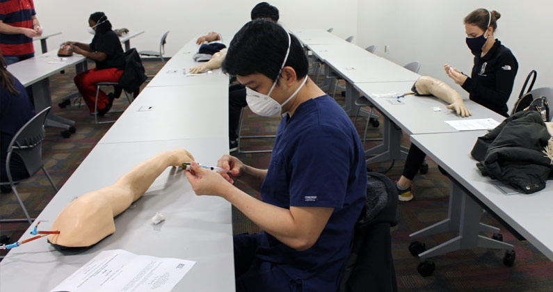 A medical student practices using a syringe to administer the COVID-19 vaccine.