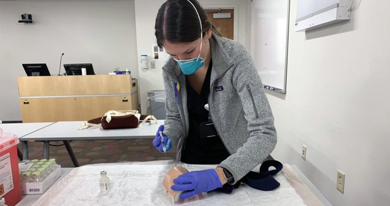 A pharmacy student practices giving a COVID-19 vaccination to mannequin arm.