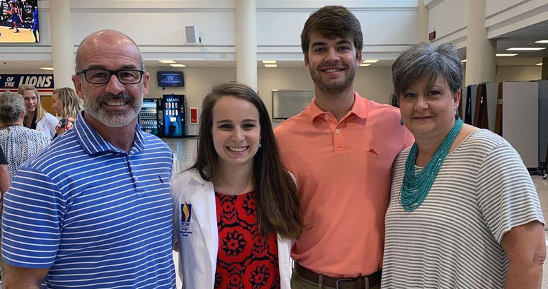 PCOM Georgia Doctor of Physical Therapy graduate Tatum Wilson, DPT, smiles and dons her physician white coat as she poses with family.