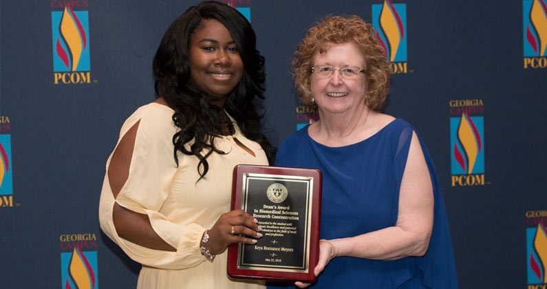 Mary Owen, JD, PhD, CS, smiles with a female med student while holding an award plaque.